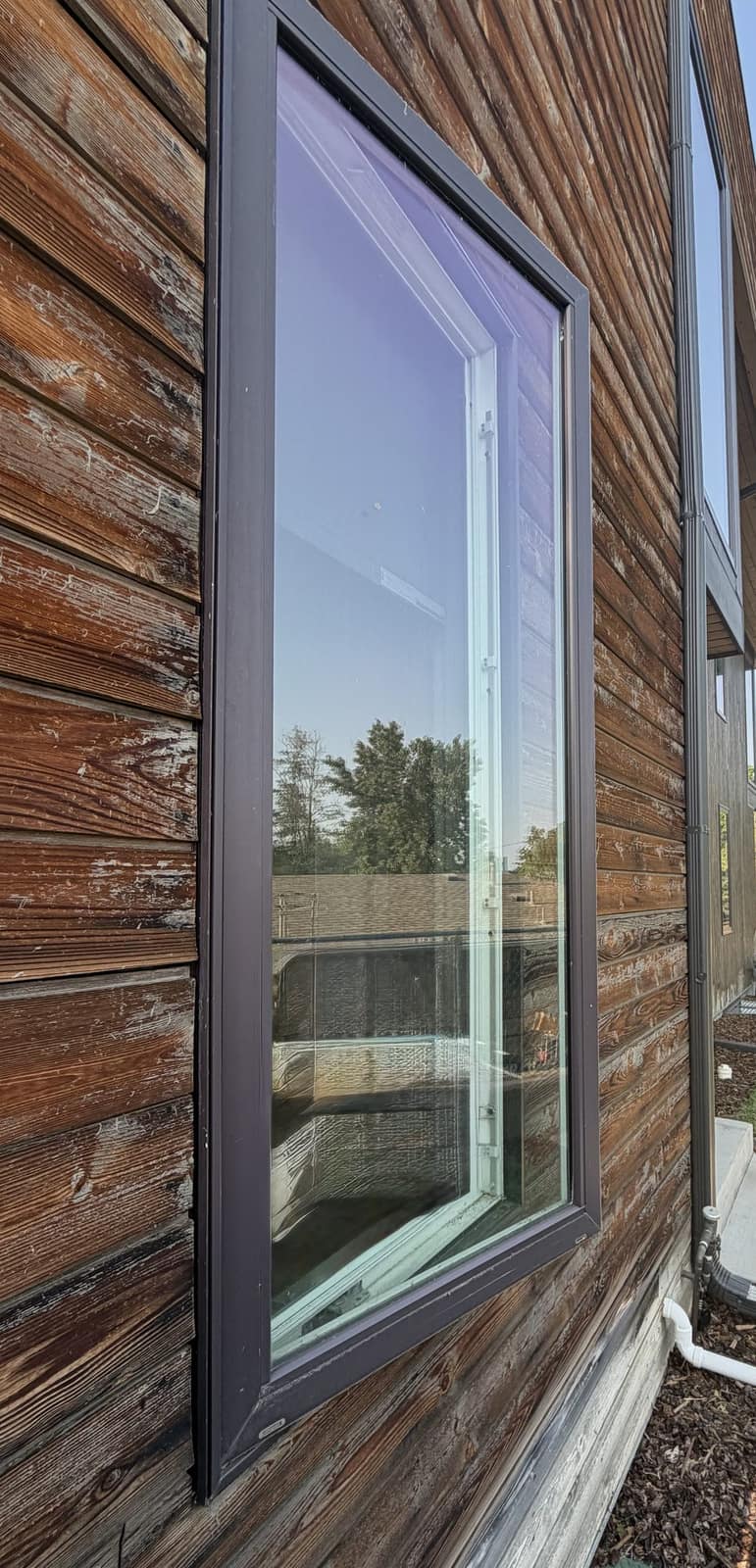 Close-up of a dark-framed casement window on a wood-sided Colorado home