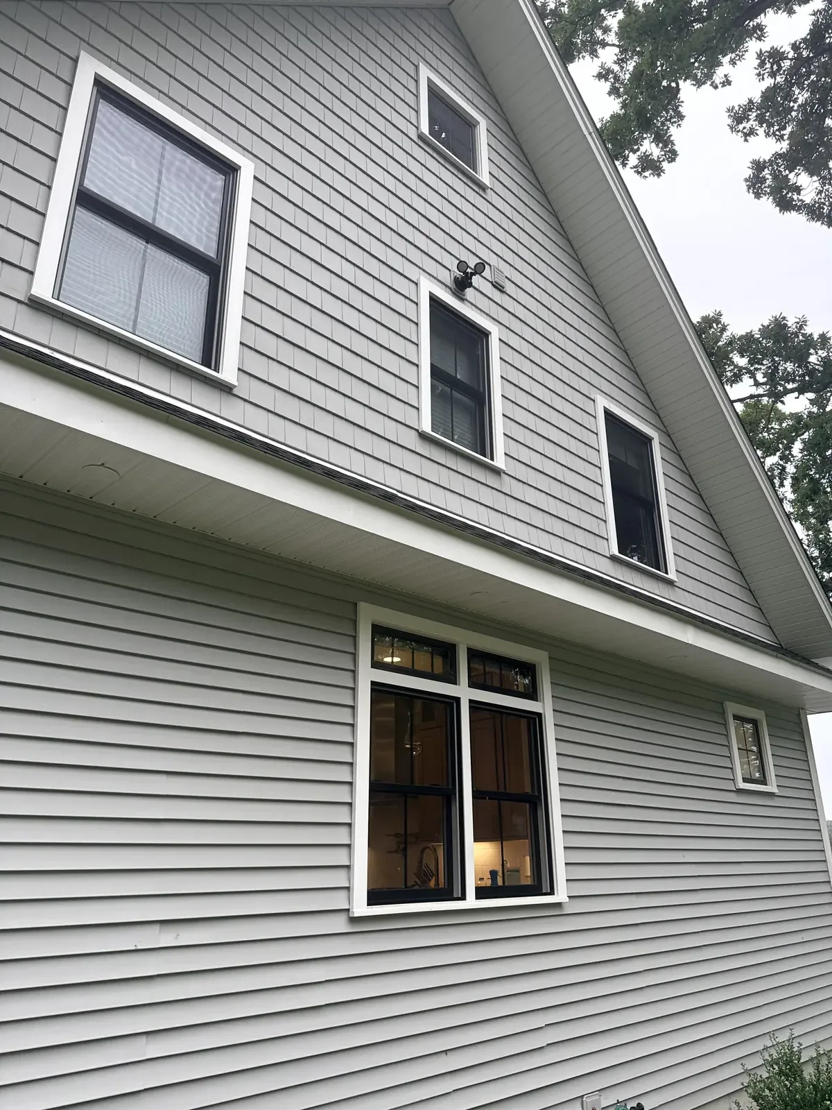 Angled view of black-framed double-hung windows and a transom kitchen window on a two-story home